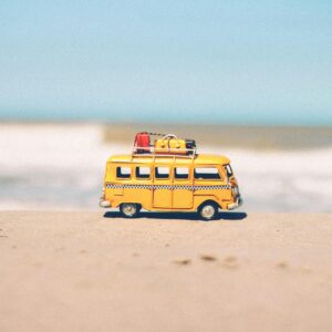 A vibrant yellow toy van sits on a sandy beach with an ocean backdrop, symbolizing fun travel adventures.