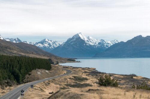 Breathtaking view of Mount Cook with a winding road, lake, and snow-capped peaks in New Zealand.