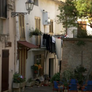 Quiet Italian street scene with laundry hanging by a charming courtyard with chairs and plants.