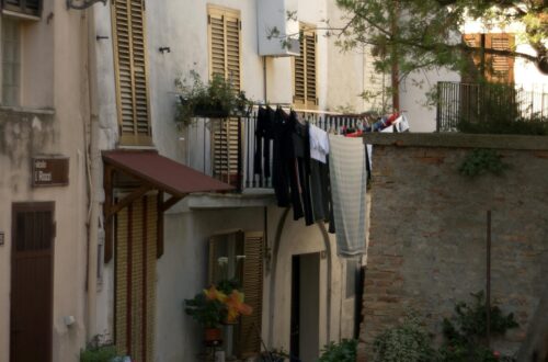 Quiet Italian street scene with laundry hanging by a charming courtyard with chairs and plants.