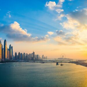 Stunning view of Dubai's skyline and waterfront during golden hour with glowing skyscrapers reflecting on the water.