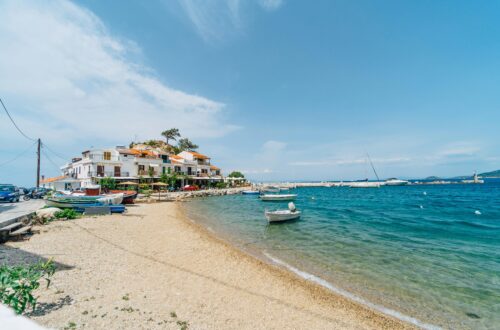 Charming beachfront in Kokkari, Greece with boats and coastal houses under a clear blue sky.