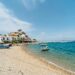 Charming beachfront in Kokkari, Greece with boats and coastal houses under a clear blue sky.