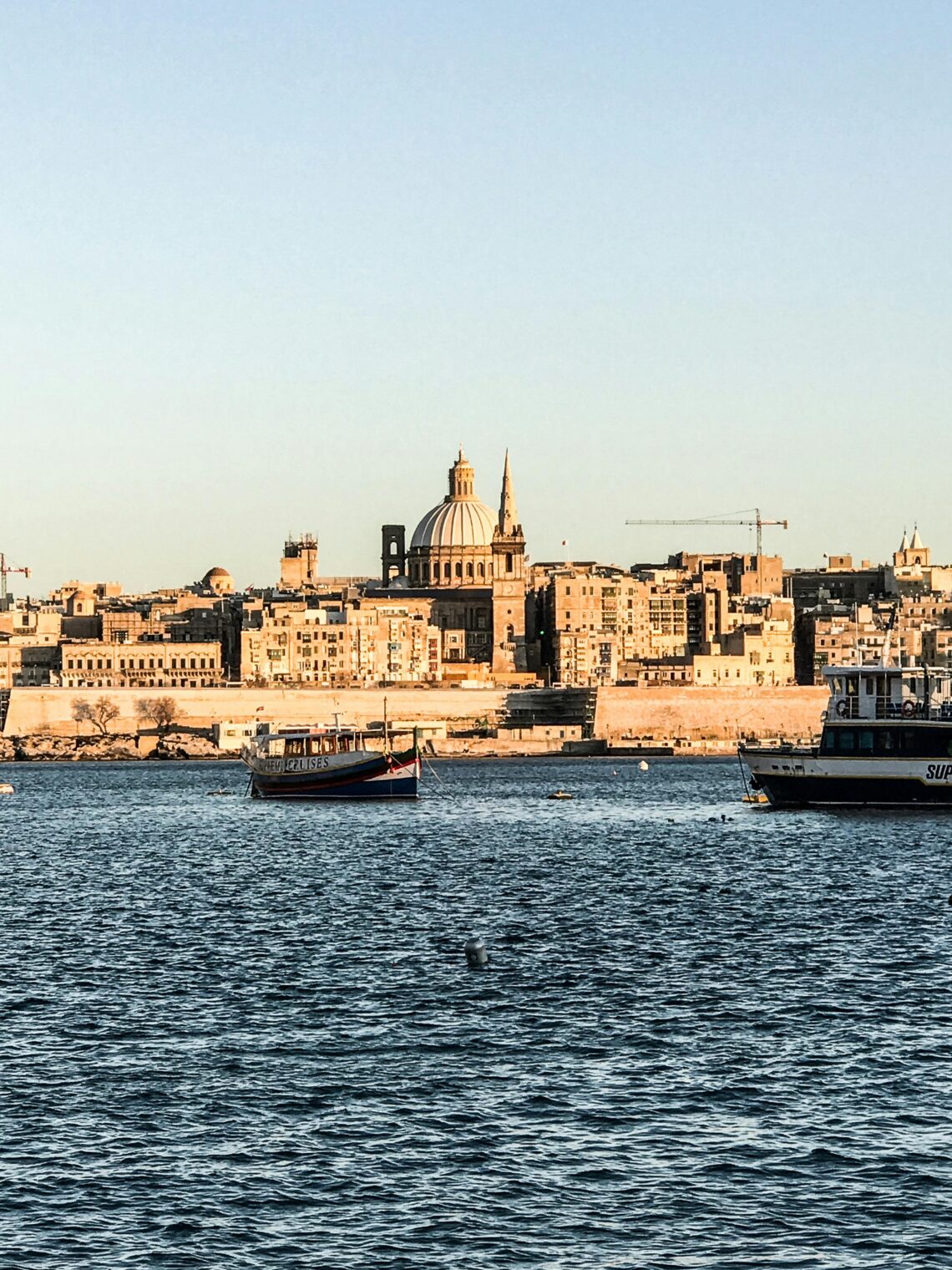 A picturesque view of Valletta's waterfront with historic architecture and boats, under clear skies.