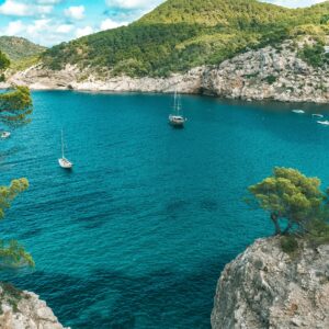 Sailboats drift in a stunning turquoise bay surrounded by rocky cliffs in Ibiza, Spain.