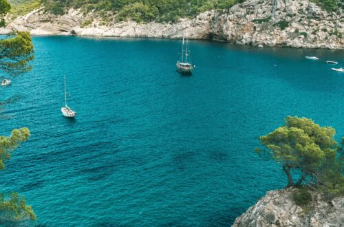 Sailboats drift in a stunning turquoise bay surrounded by rocky cliffs in Ibiza, Spain.