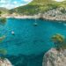 Sailboats drift in a stunning turquoise bay surrounded by rocky cliffs in Ibiza, Spain.