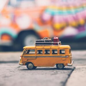 Close-up of a toy Volkswagen van with luggage, set against a colorful street backdrop, evoking summer travel vibes.