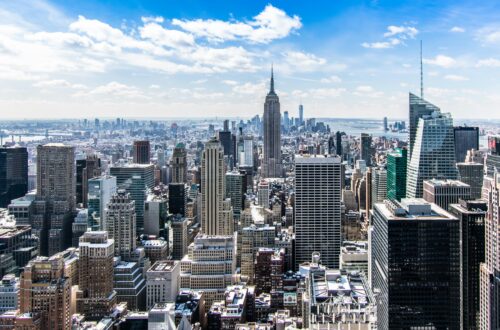 A stunning aerial view of New York City's skyline featuring the iconic Empire State Building under a bright blue sky.