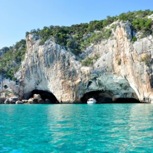 A boat enters a stunning cave along the rocky coastline of the Mediterranean Sea.