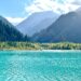 Beautiful turquoise lake surrounded by mountains and forests in Kazakhstan, under a clear blue sky.